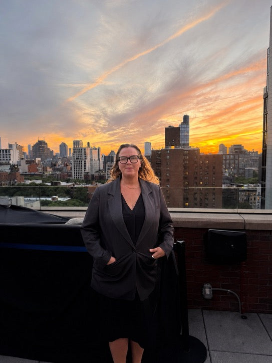 Woman standing on a rooftop with a city skyline and sunset in the background