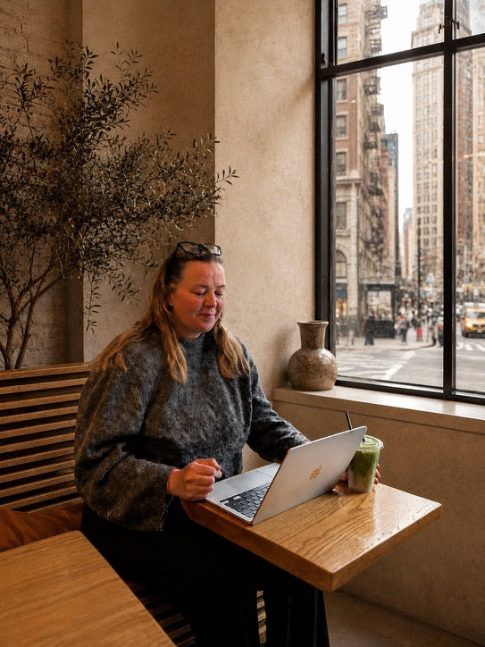Person using a laptop at a table with a cityscape view through a window.